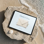Coastal beach wedding website template shown on iPad, cream lace envelope with seashell seal on beach rock