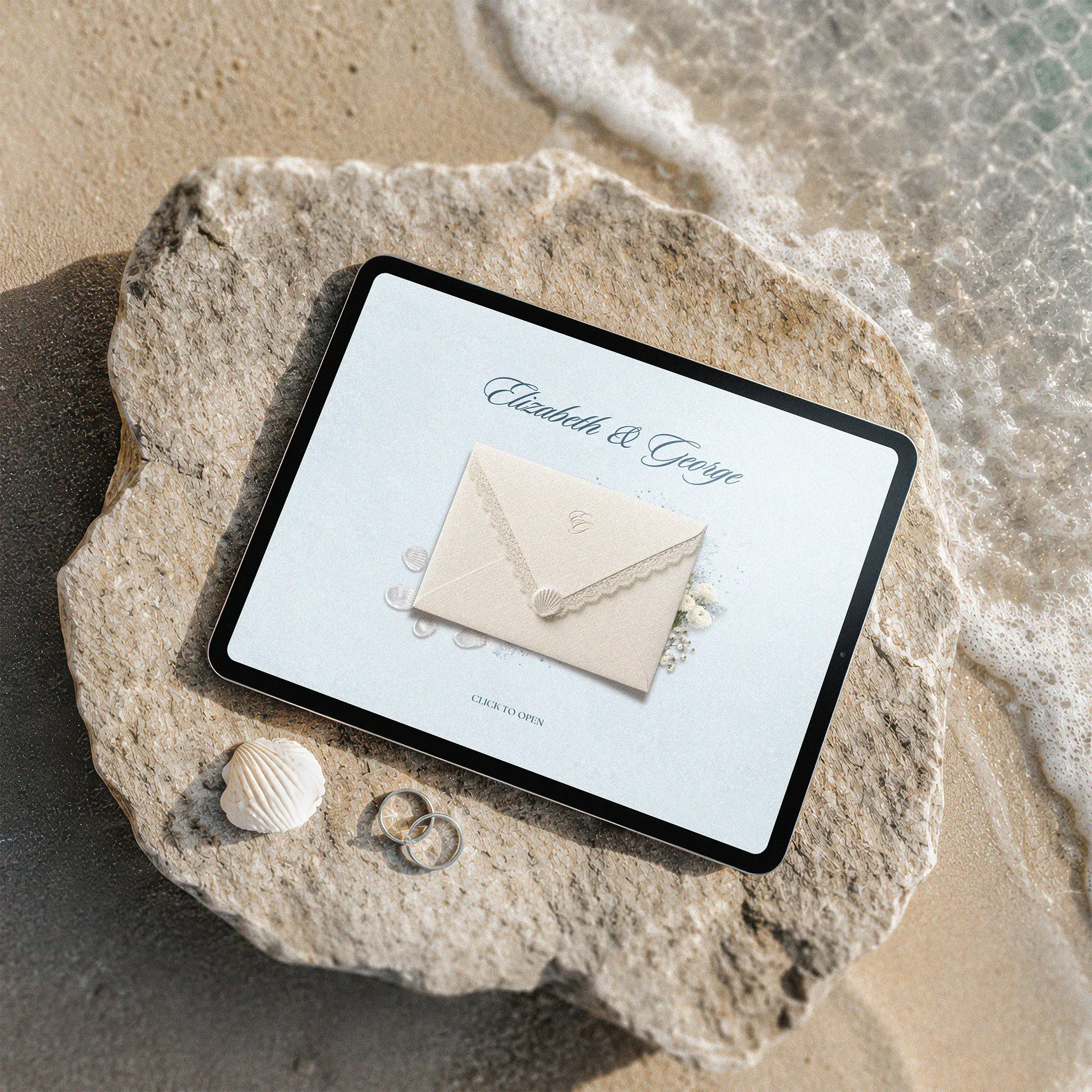 Coastal beach wedding website template shown on iPad, cream lace envelope with seashell seal on beach rock